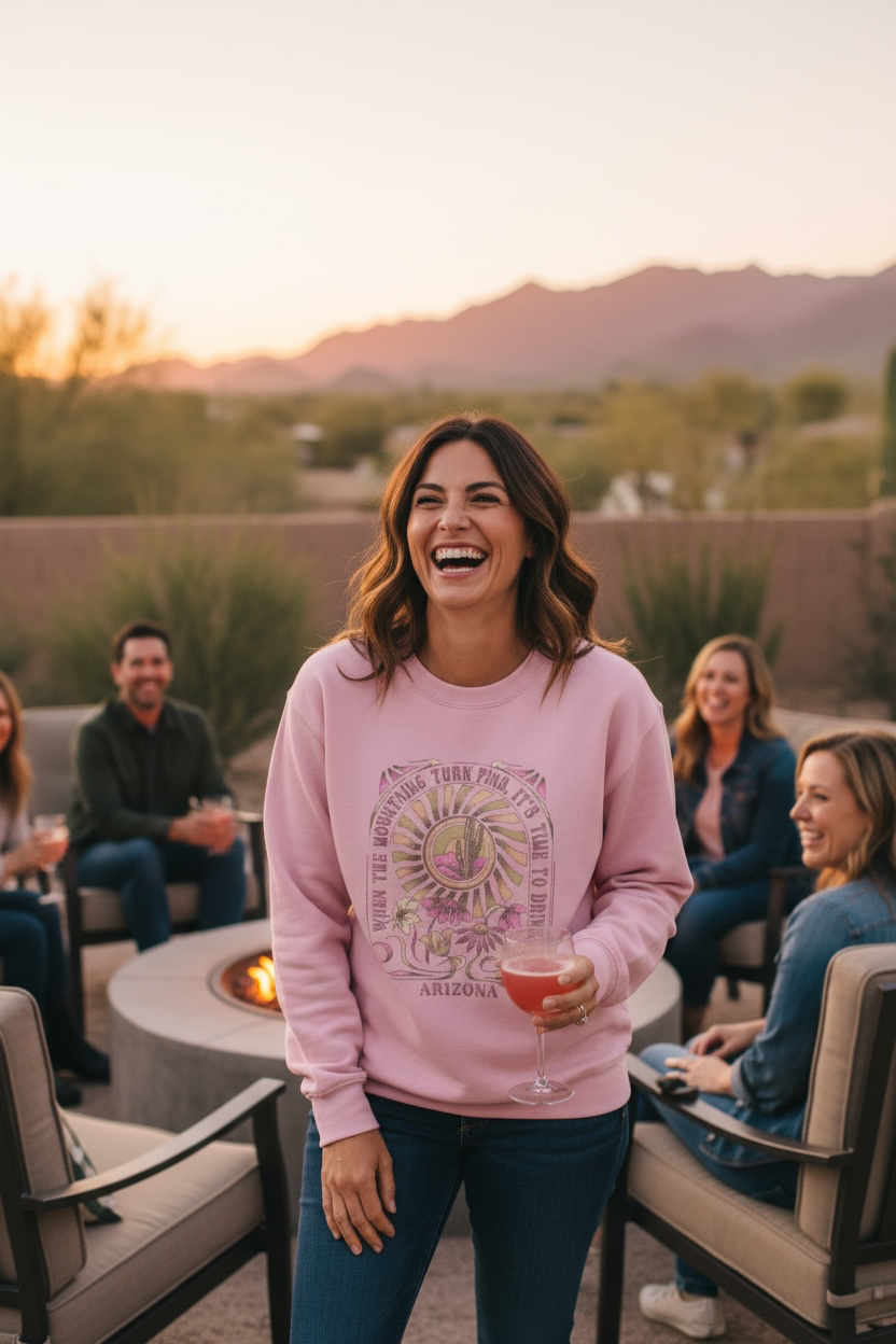 Pink Arizona sweatshirt featuring a weathered crew-flower design with cactus and sunset graphic, worn while laughing at an outdoor火 pit gathering.