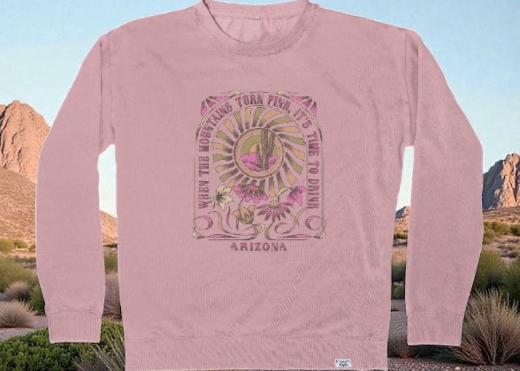 Pink corduroy sweatshirt featuring retro Arizona mountain sunset graphic with flora and text "When the Mountains Turn Pink, It's Time to Drink" against desert backdrop.